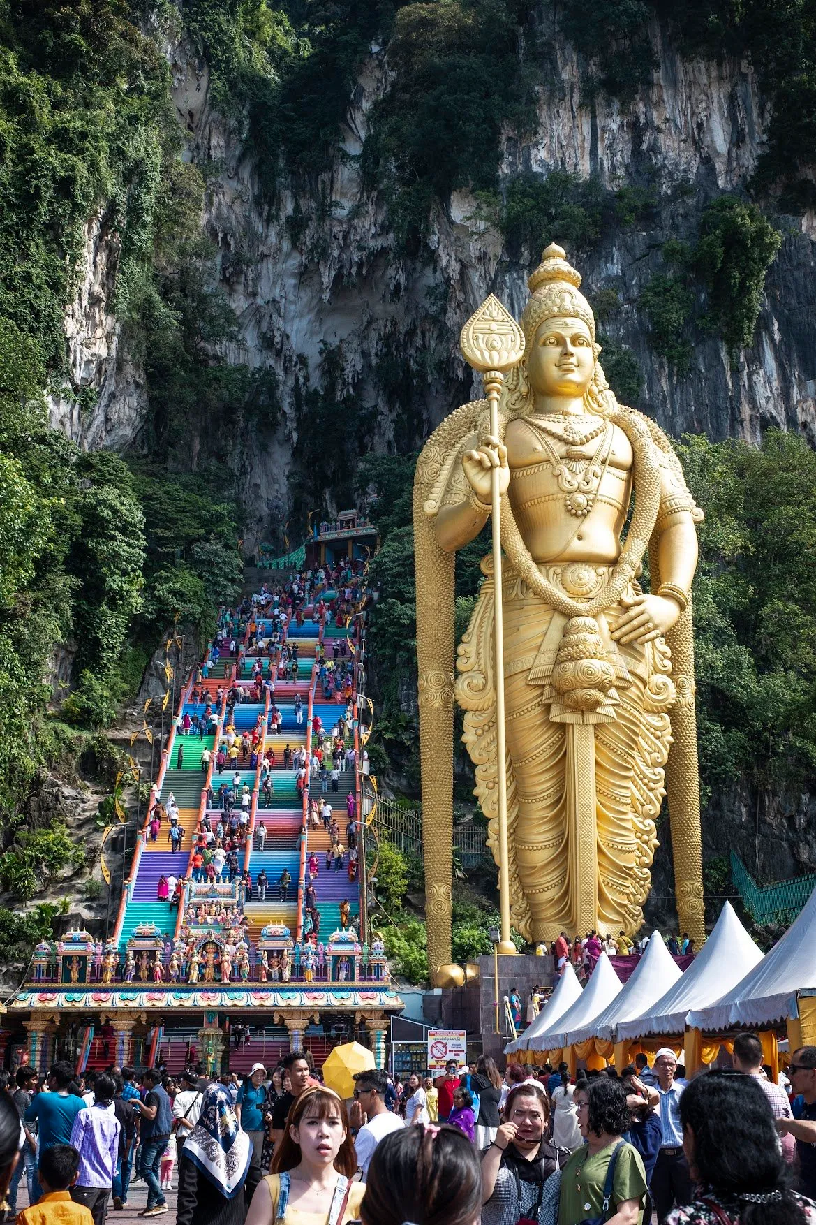 The gold statue of Lord Murugan beside the rainbow-painted stairway climbing to the limestone caves
