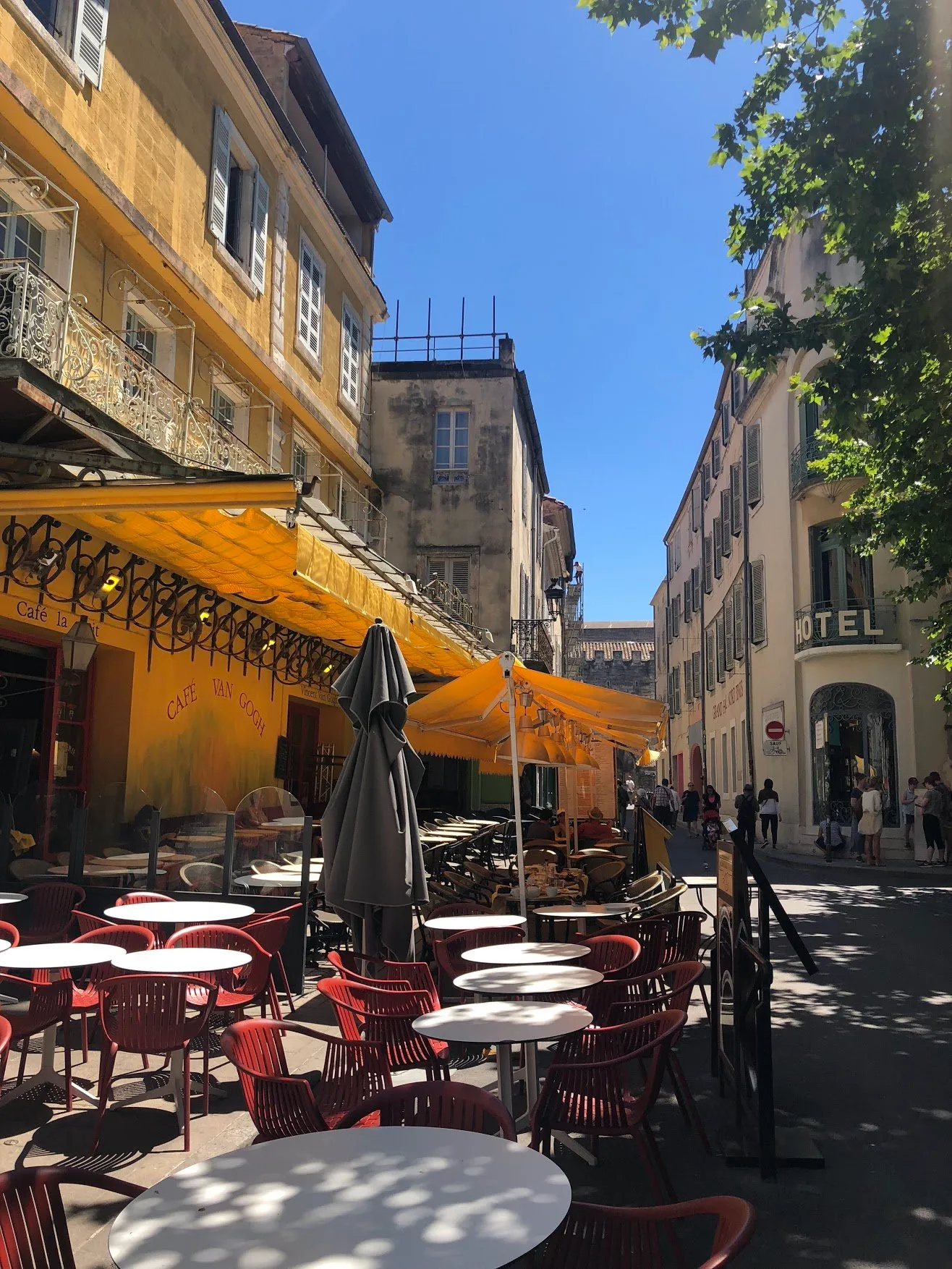 Yellow awnings over café tables on a narrow sunlit street in Arles