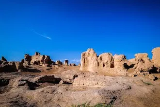 Eroded earthen walls of the ruined city rising from bare rock against a deep blue sky
