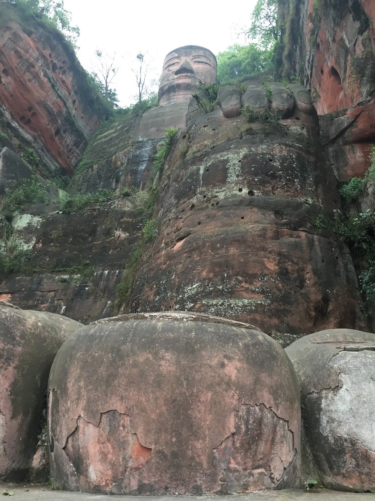 Looking up the carved red cliff to the Giant Buddha’s head, its huge stone feet in the foreground
