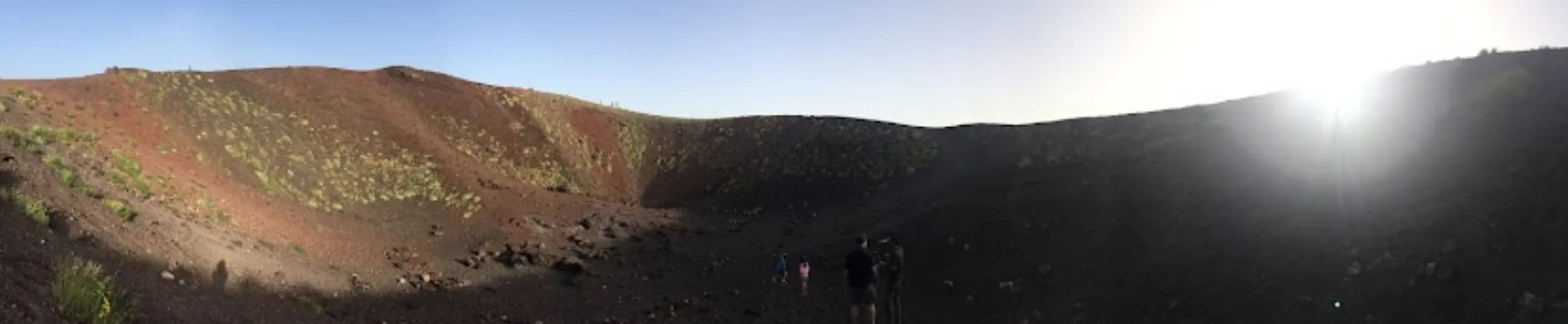 A wide view along the dark crater rim of Vesuvius, two walkers small on the path