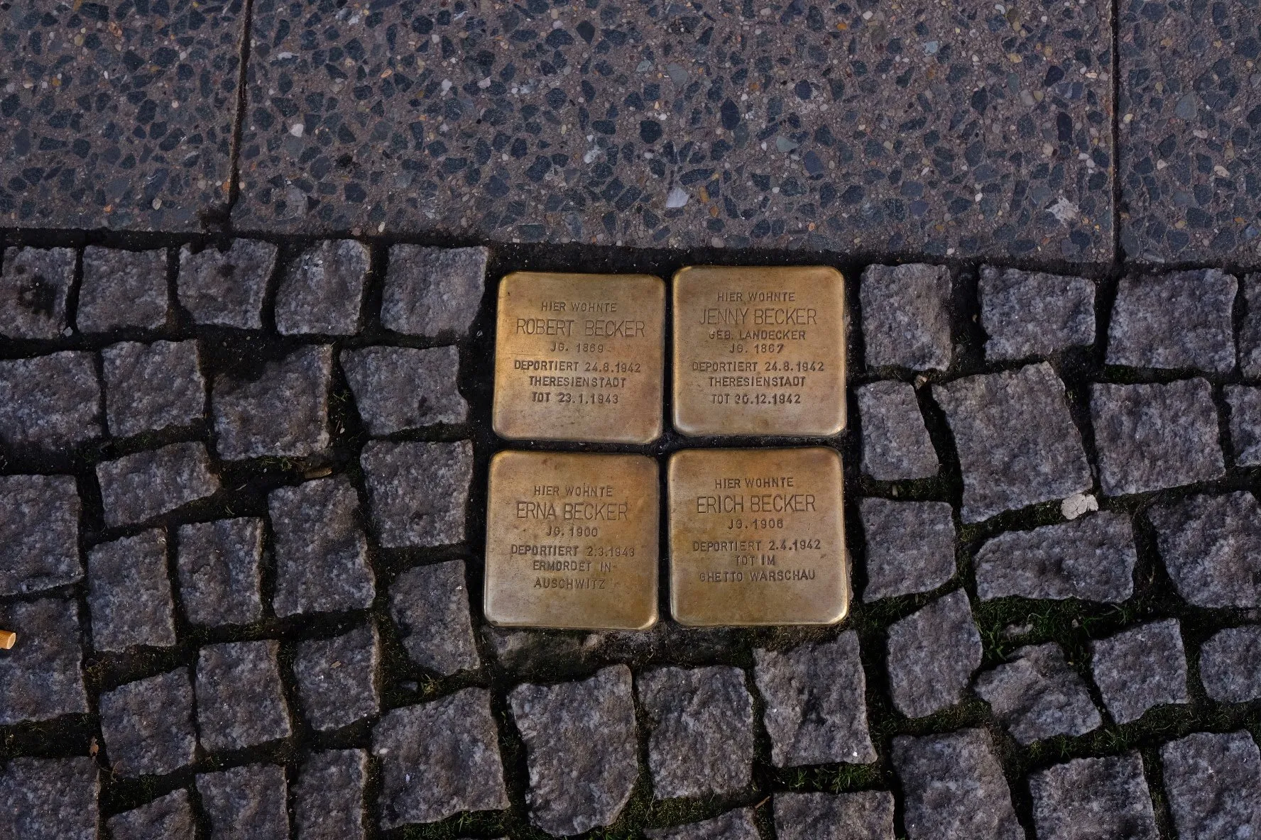 Four brass memorial blocks set flush into the cobblestones at the edge of a pavement