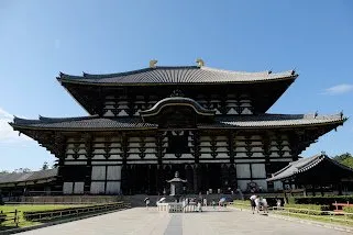 The temple’s broad wooden hall and sweeping tiled roof under a clear sky, visitors crossing the courtyard